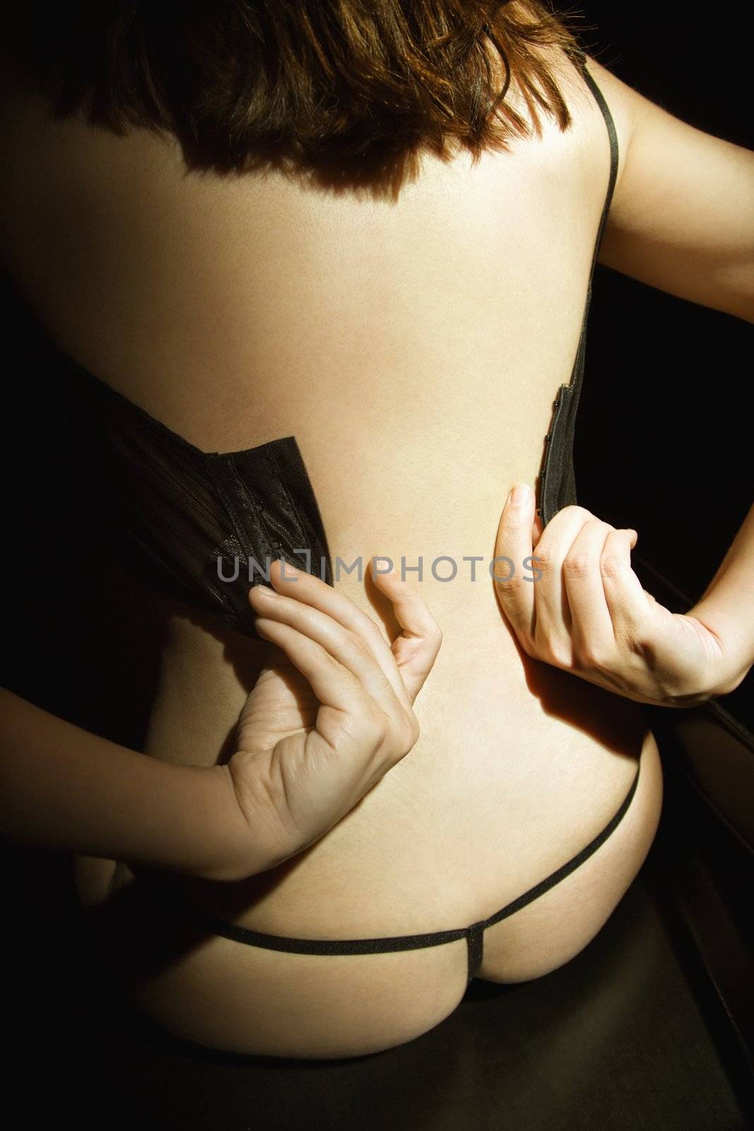Back view of attractive Caucasian woman in lingerie undressing.