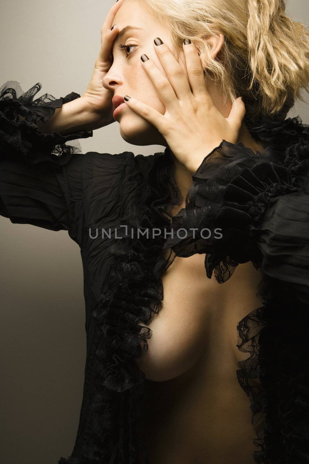 Sexy partially nude Caucasian woman looking to side with hands on face.