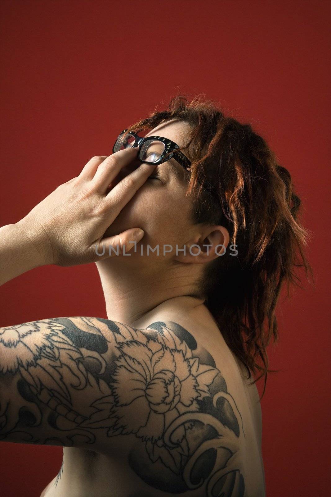 Adult woman with tattoos rubbng her eyes.