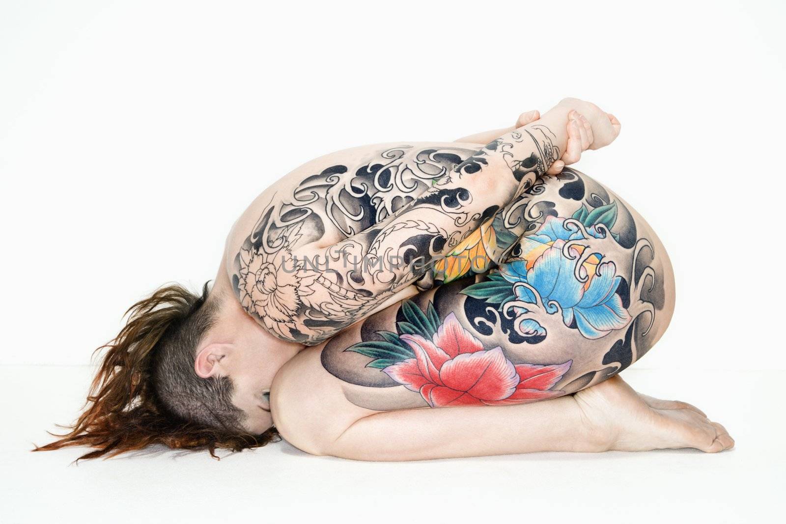Nude caucasian woman with tattoos sitting on floor.