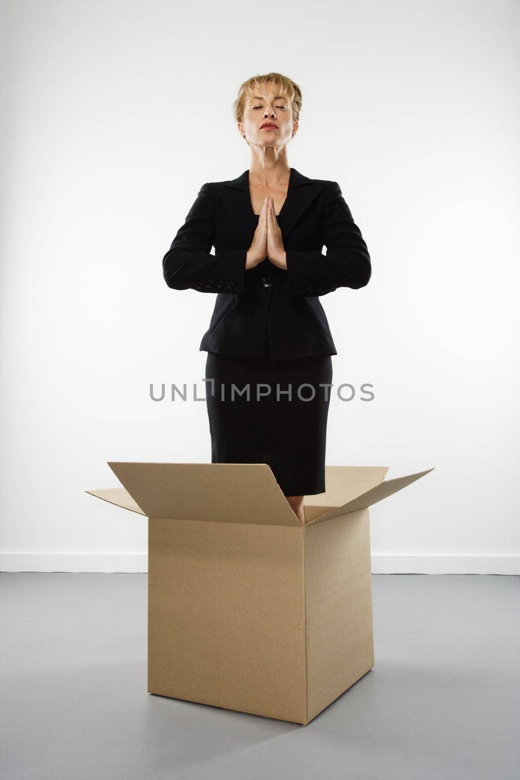 Caucasian businesswoman standing inside cardboard box meditating with eyes closed.