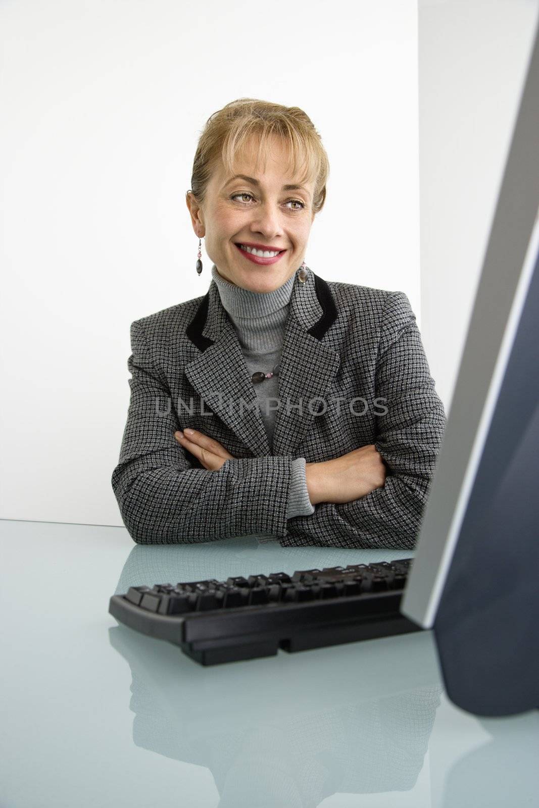 Caucasian woman looking at computer and smiling with arms crossed.