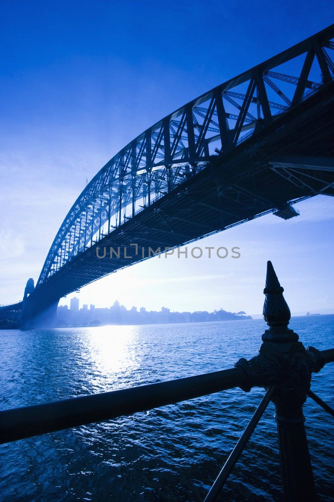 Low angle view of Sydney Harbour Bridge at dusk with harbour and distant Sydney skyline, Australia.