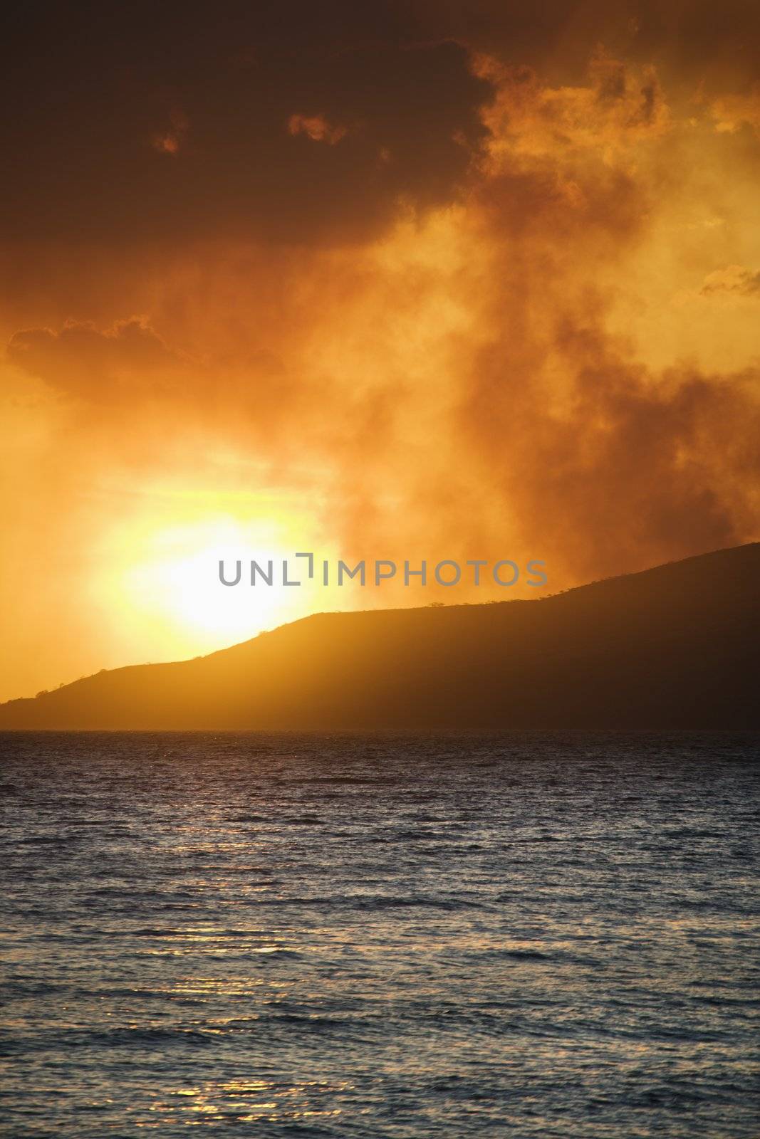 Sun setting over island with ocean on Maui, Hawaii.