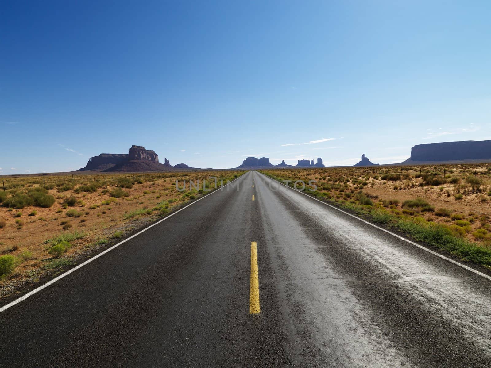 Open road in scenic desert landscape with distant mountains and mesas.