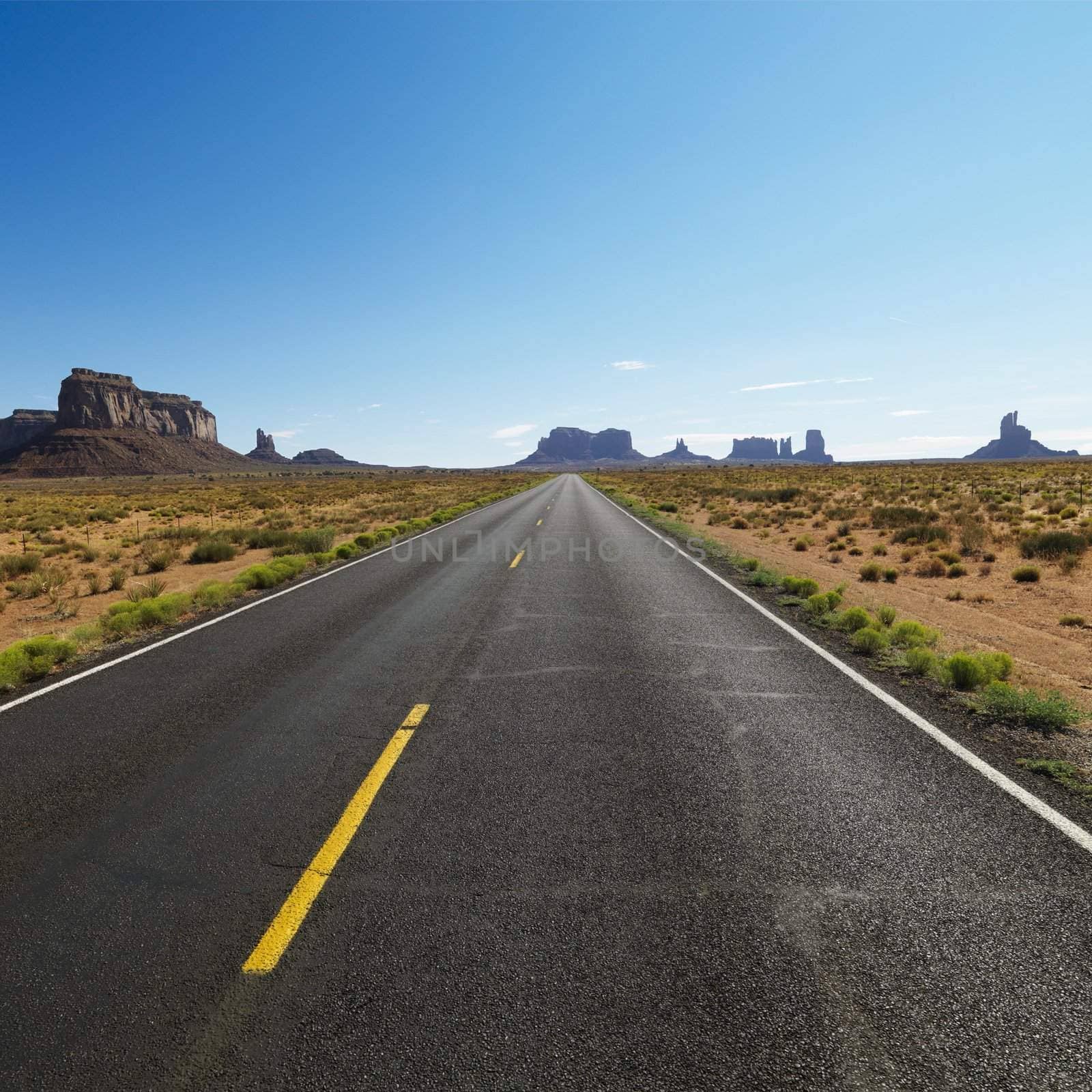 Open road in scenic desert landscape with distant mountains and mesas.