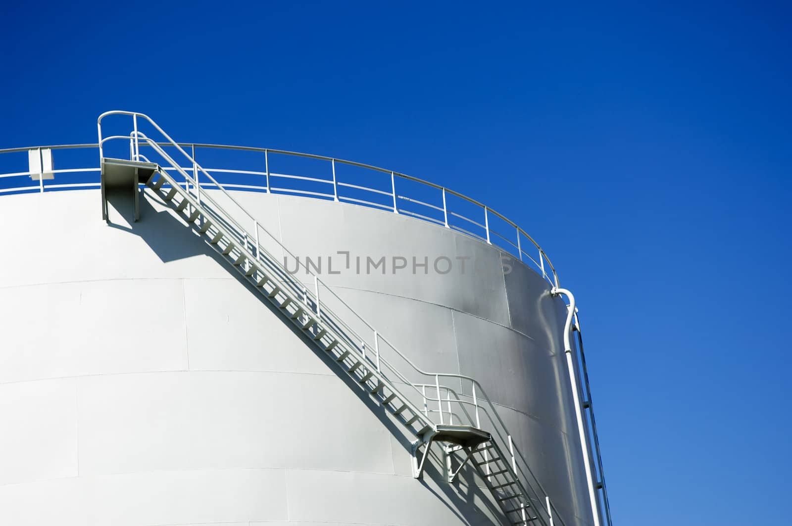 Oil reservoir detail with access ladder against a blue sky