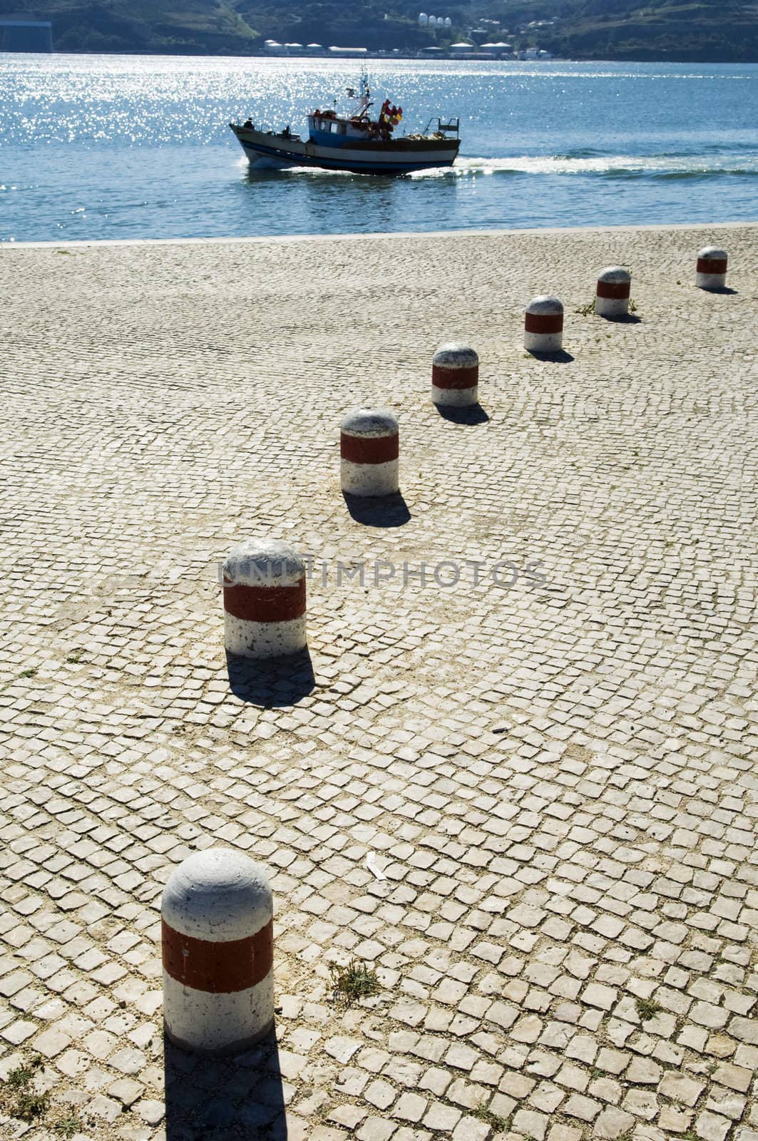 A view of a small fishing boat as it passes a large cobblestone quay on its way out of the harbor on the Tagus River in Lisbon, Portugal.