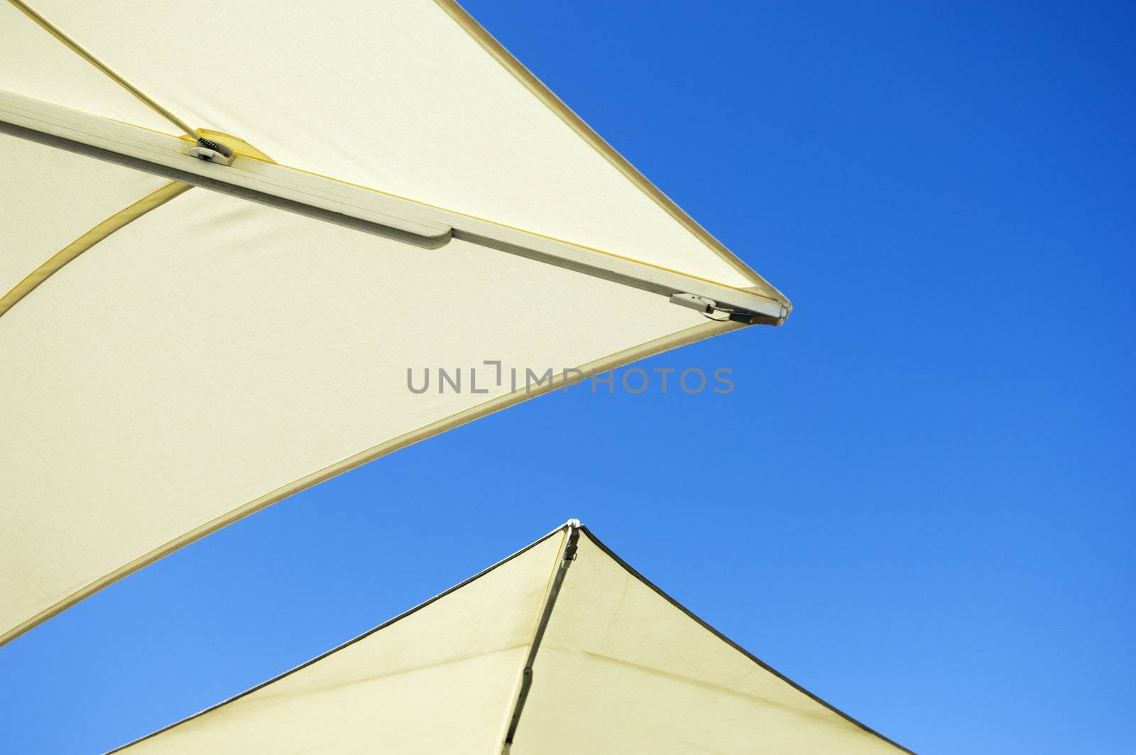 The edges of two white umbrellas in front of blue sky sunny background