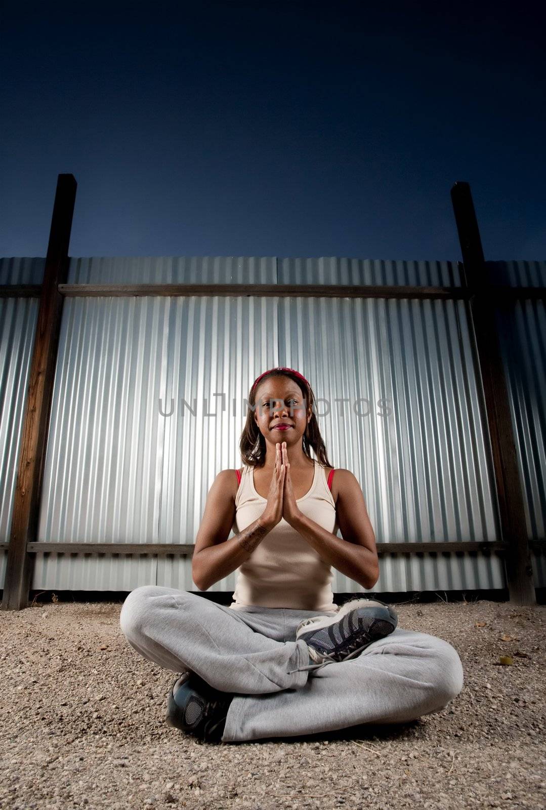 African-American woman meditating in front of corrugated metal