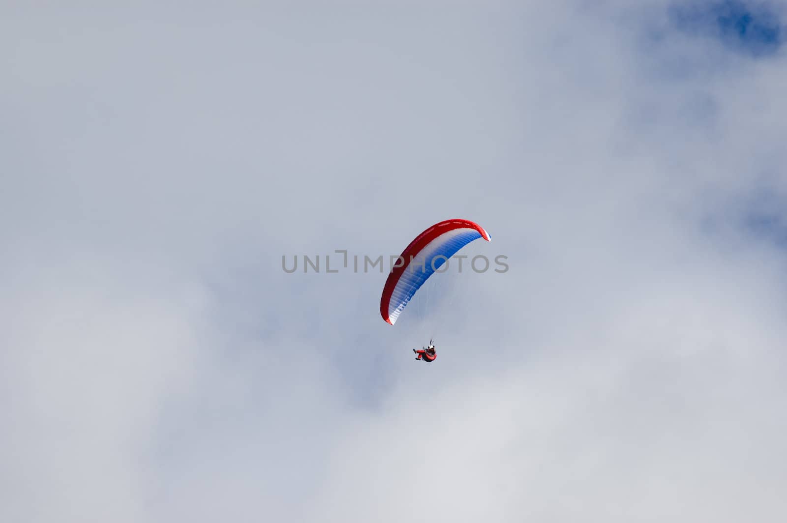 Man enjoying the ride in a blue white red paraglider