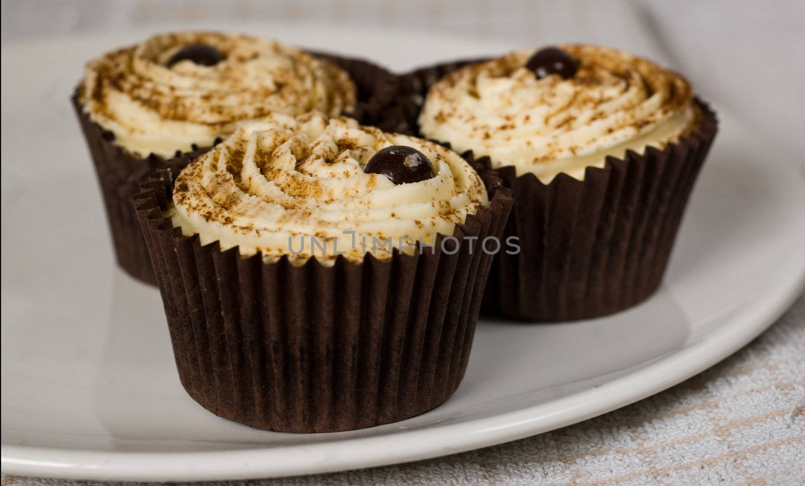 a close up of three delicious chocolate and cherry cup cakes sat upon a white plate.