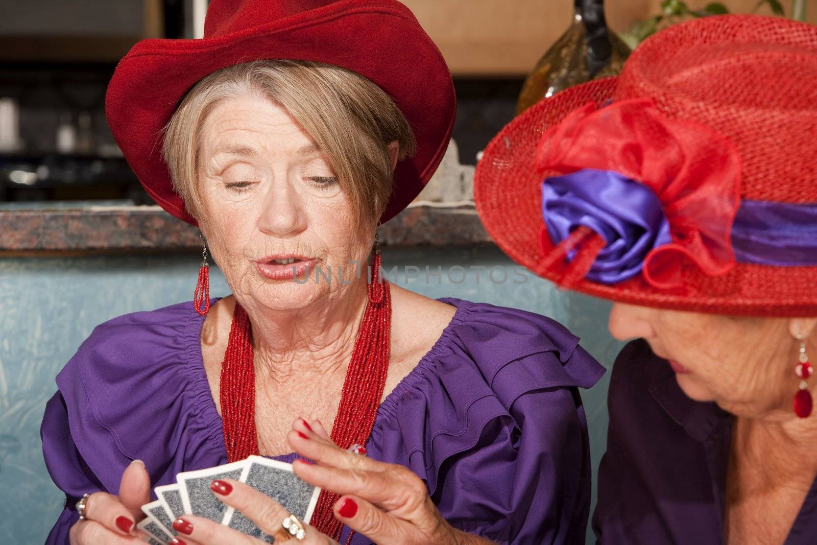 Ladies wearing red hats playing a hand of cards