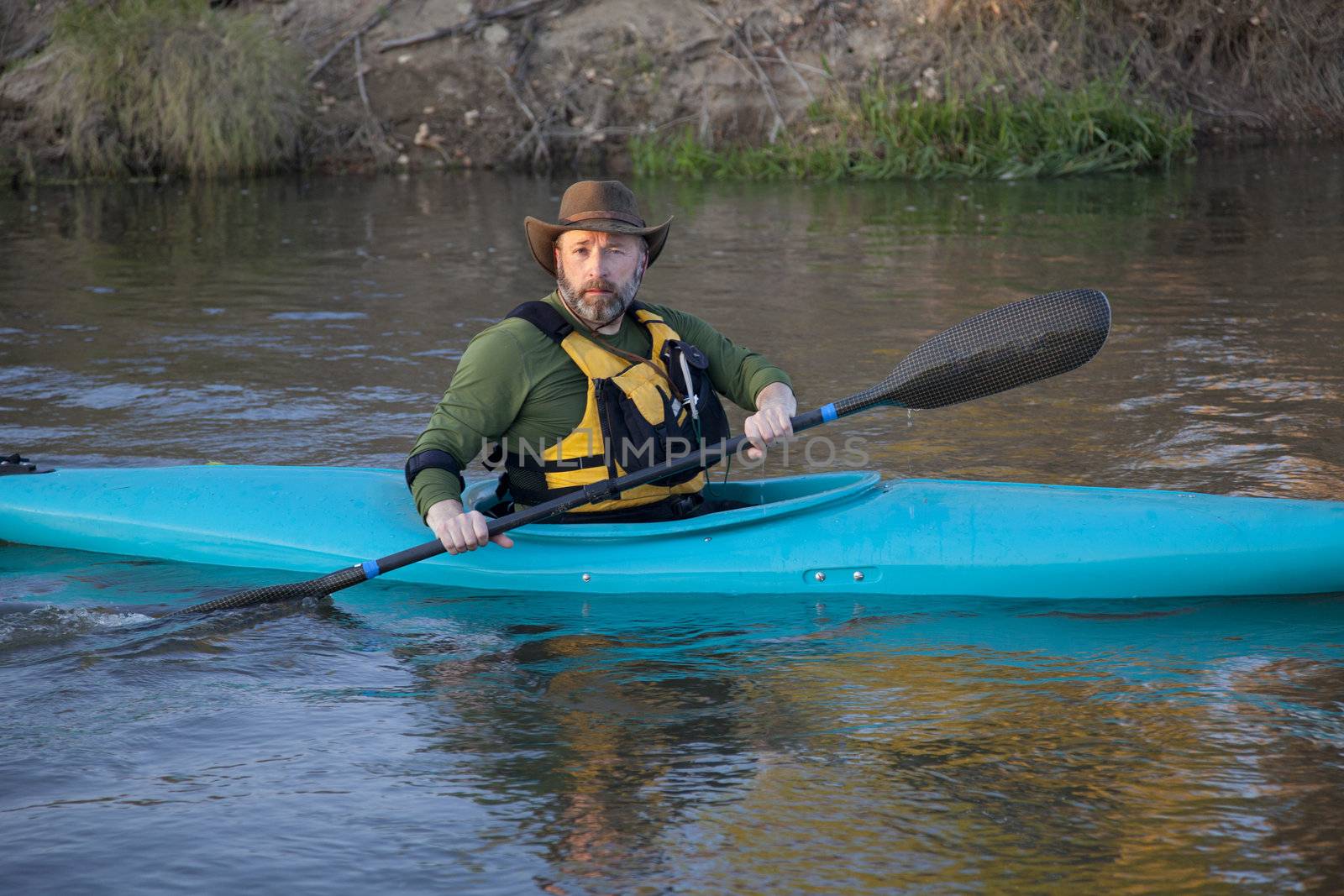 adult, male paddler, in a blue plastic whitewater kayak on a calm river