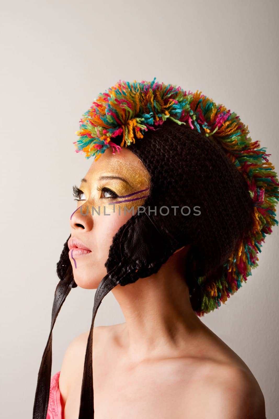 Beautiful Asian female face with a colorful mohawk hat with straps, gold and purple makeup, isolated