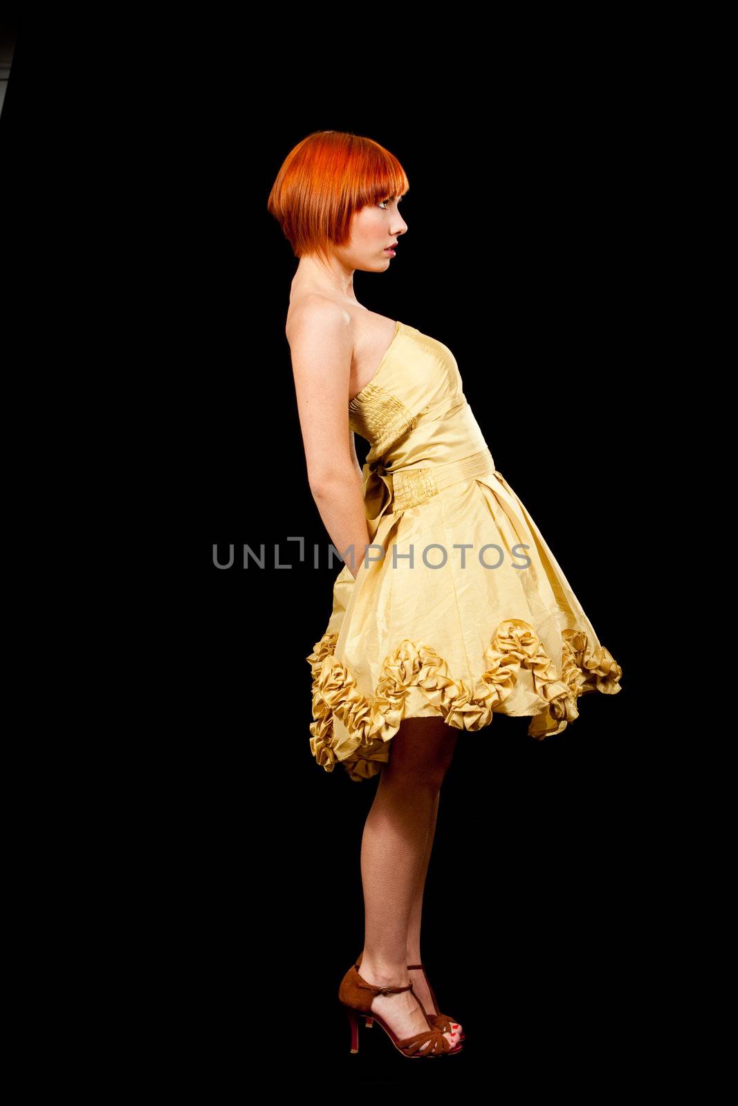 Side profile of a beautiful Caucasian redhead woman in yellow cocktail dress standing leaning backward, isolated