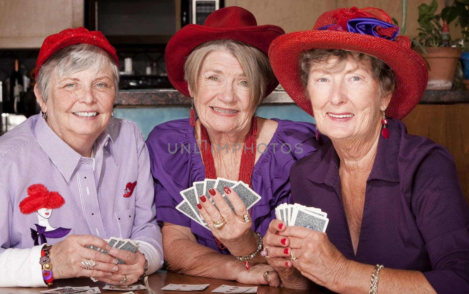 Ladies wearing red hats playing cards by Creatista