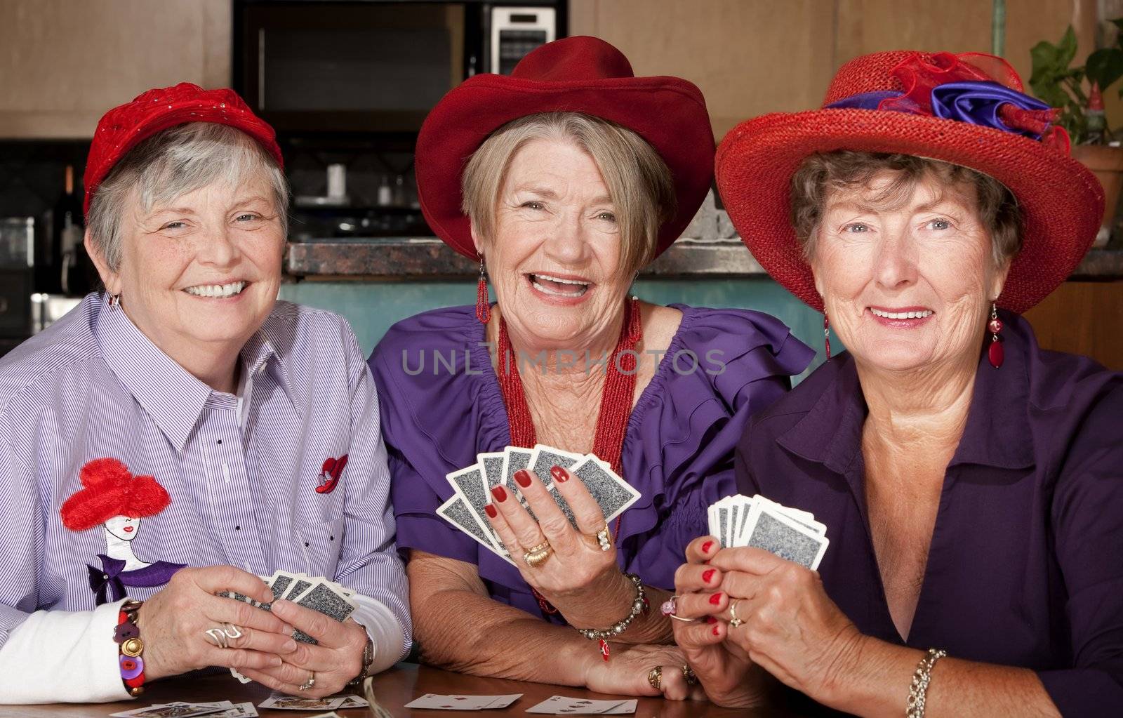 Ladies wearing red hats playing a hand of cards