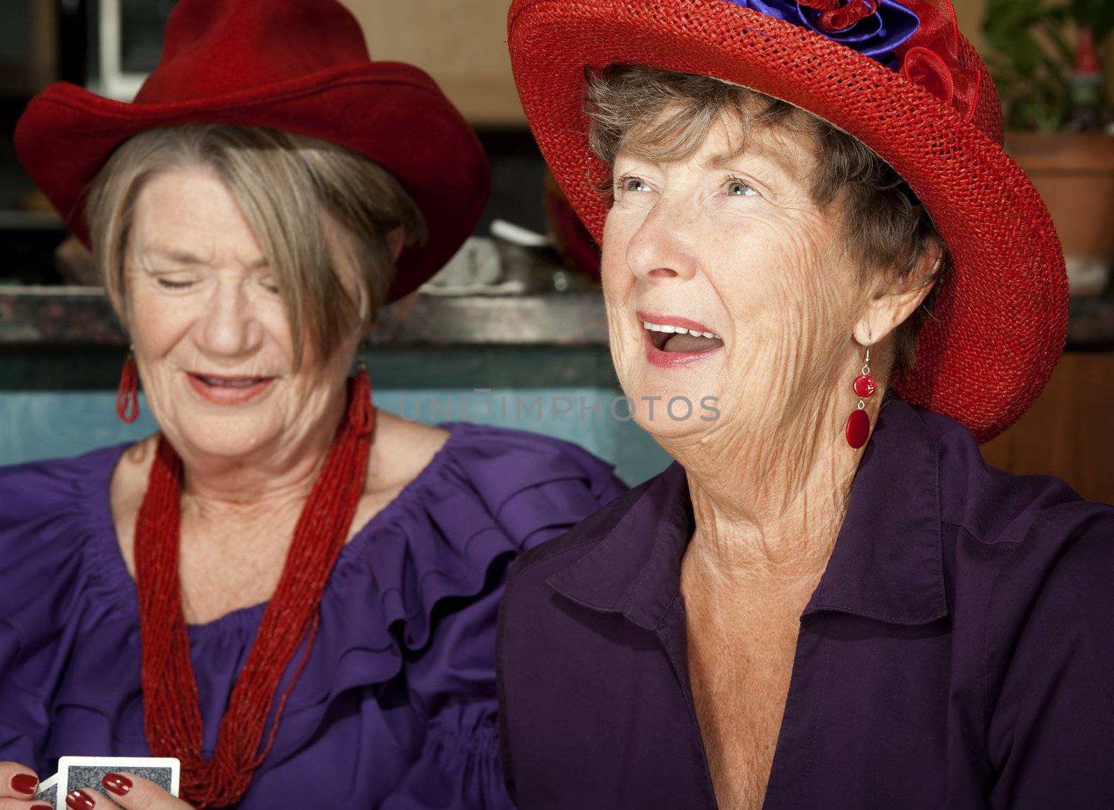 Ladies wearing red hats playing a hand of cards