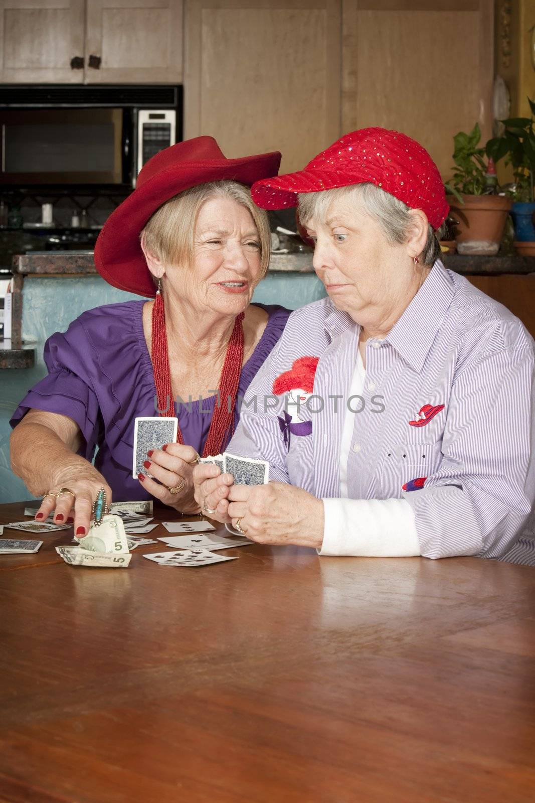 Ladies wearing red hats playing a hand of cards