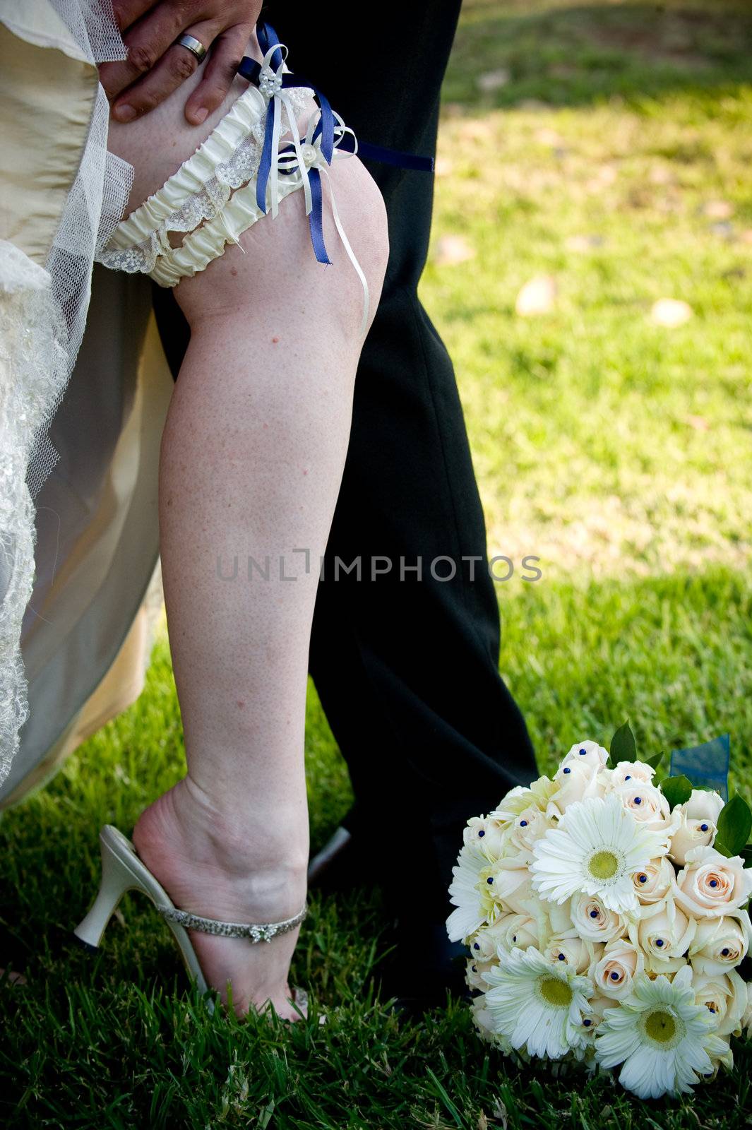 Groom’s hand on revealed bride's leg with blue and white garter exposed