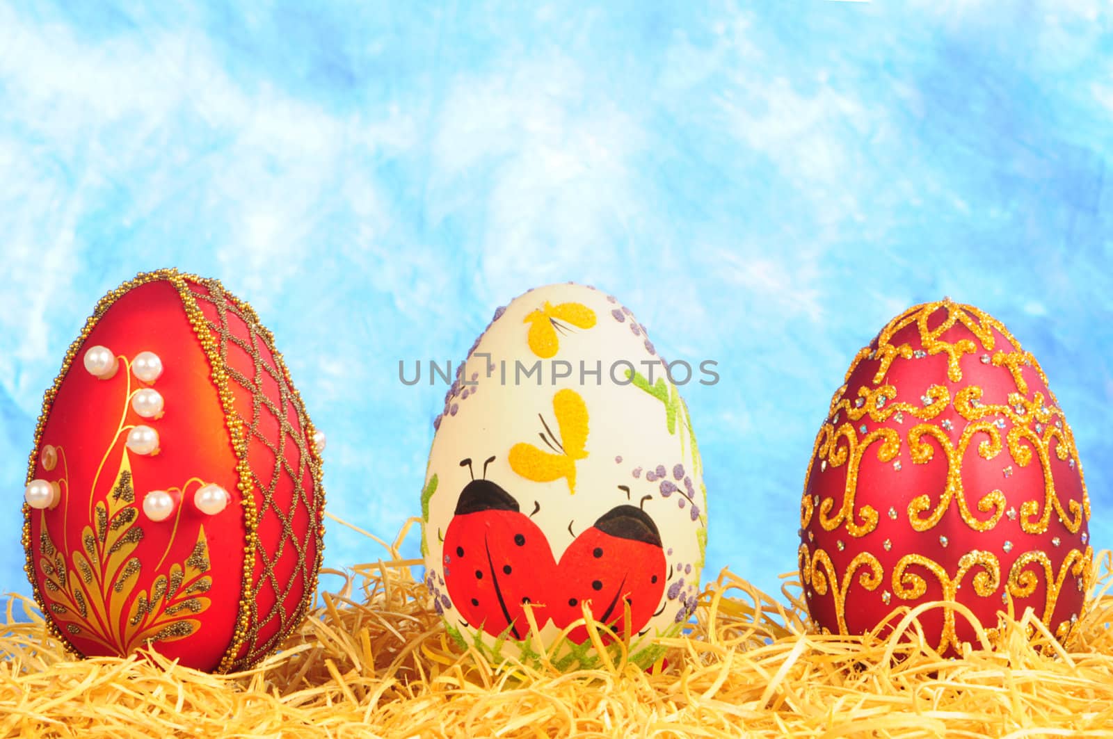 three luxury easter eggs in straw on blue background