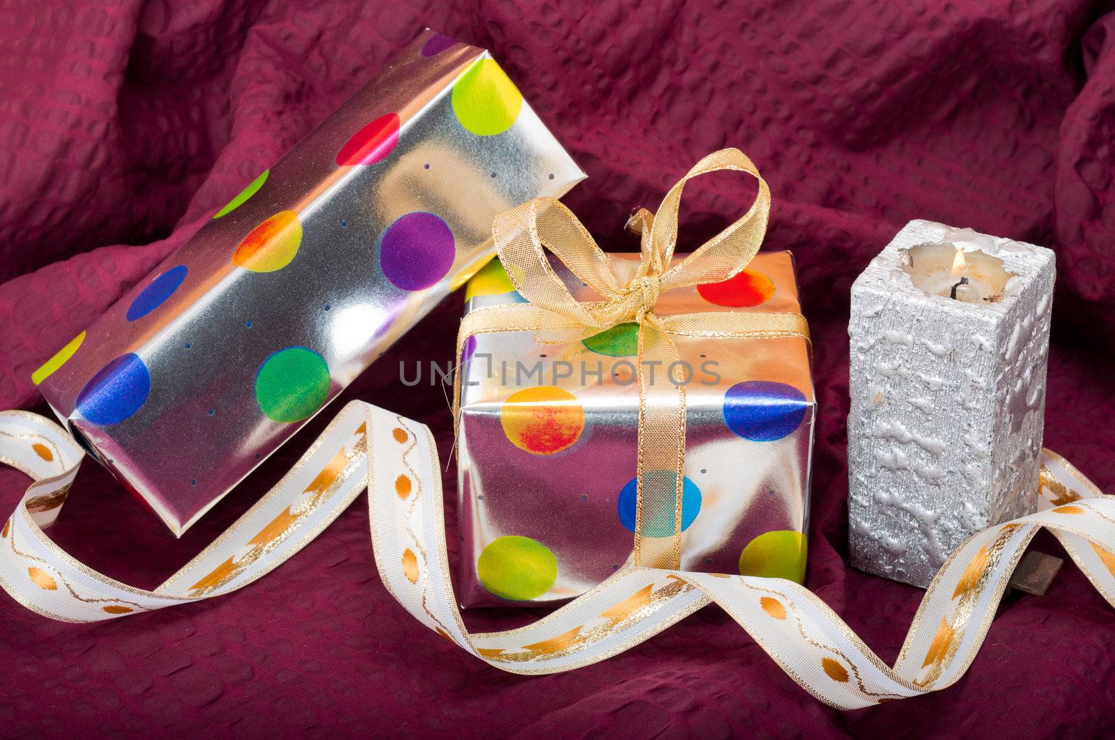 Silver gift boxes with colorful dots and ribbons and candle on burgundy background
