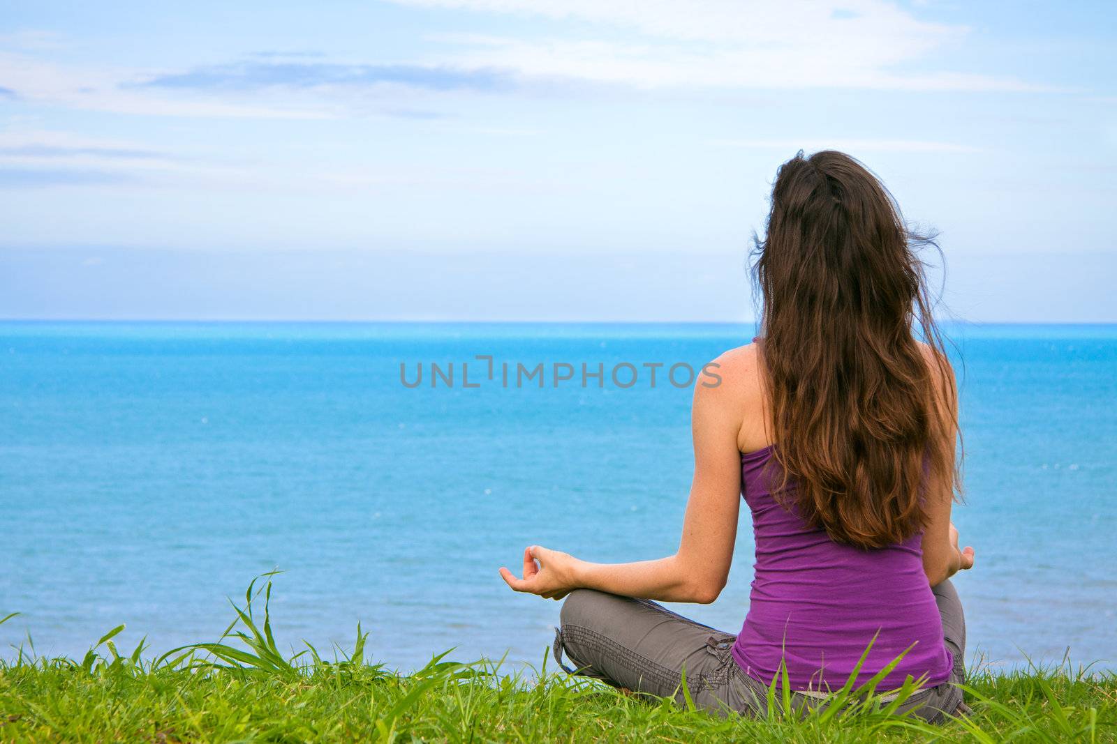 A beautiful young woman sitting meditating with a view of the ocean