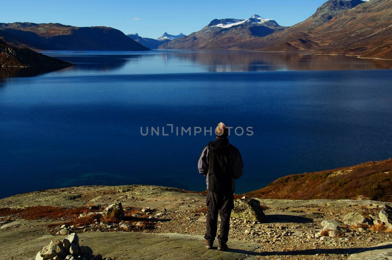 A hiker on top of a mountain with  a view over a lake