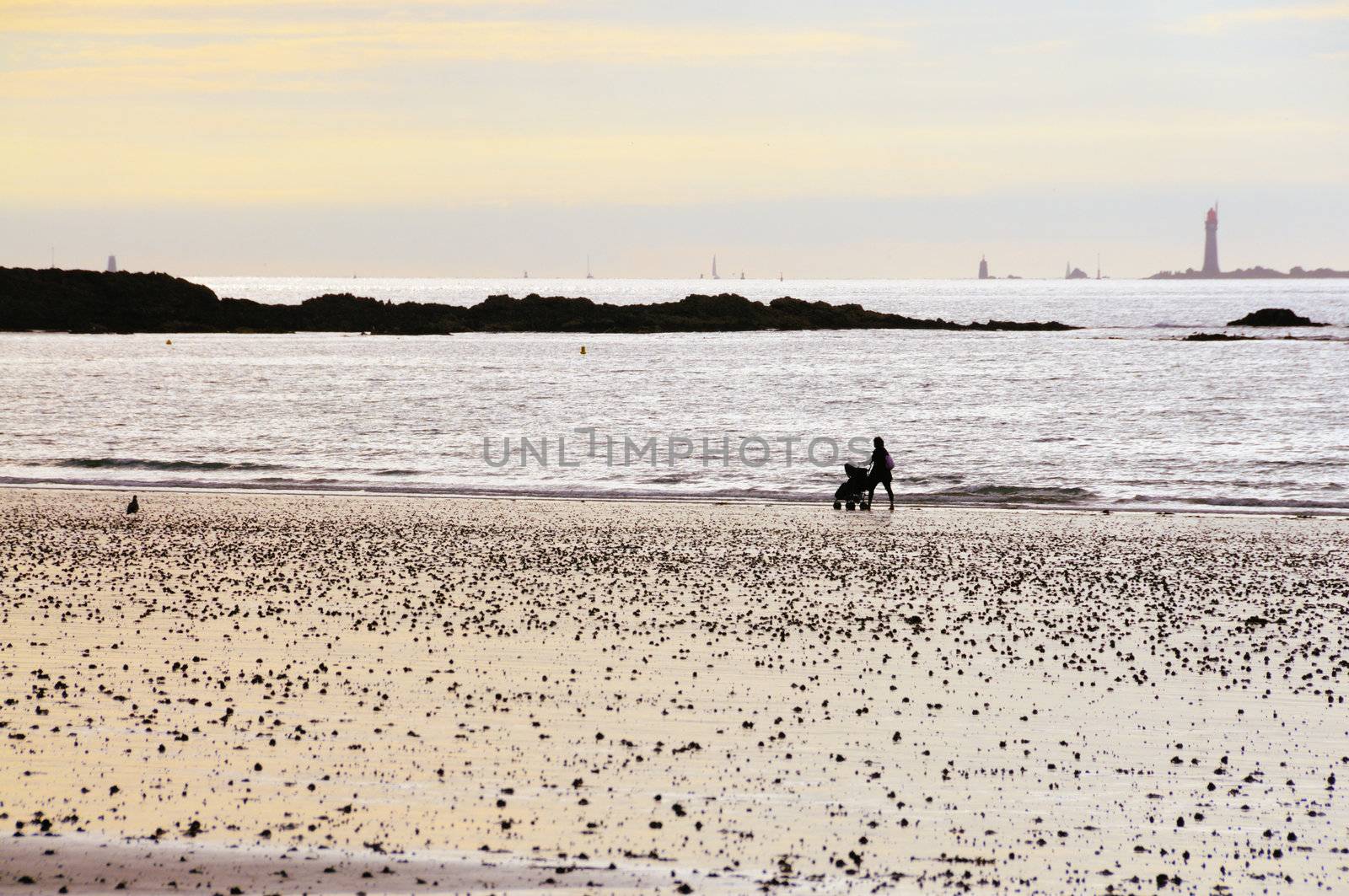 Mother pushing baby buggy along the beach of Saint-Malo in Brittany, France on a beautiful sunset.