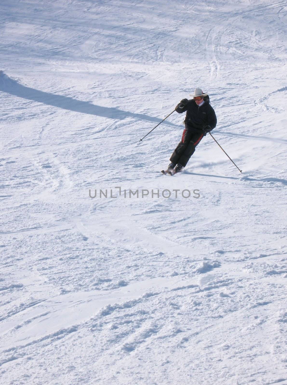 A skier coming down from the mountain, turning into a traverse to change direction, throwing up some snow.