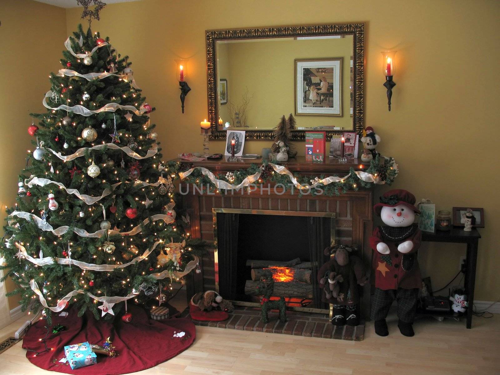 Christmas setting in a living room, with the tree all decorated, fireplace glowing, candles lit, presents around the base of the tree.