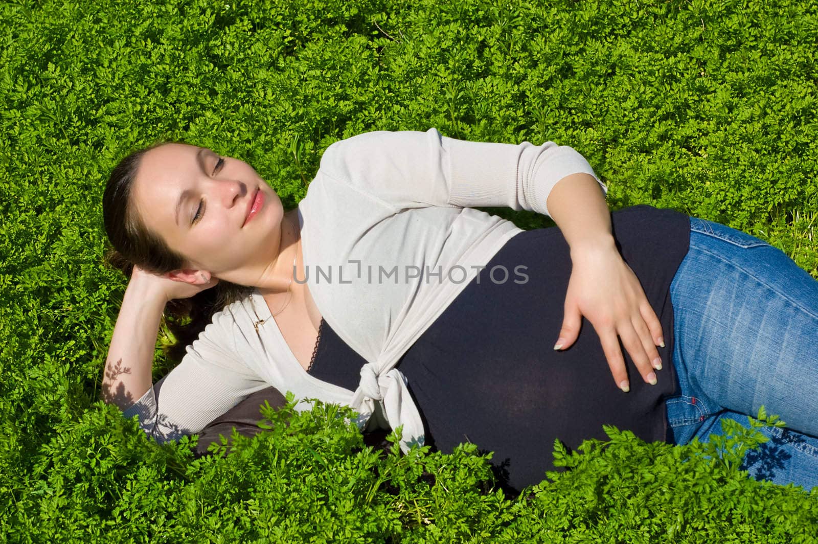 Calm pregnant woman enjoying lying in green grass