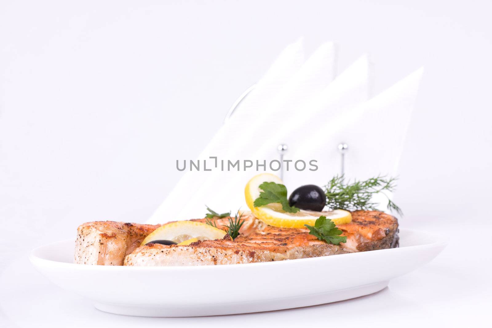 Appetizing Grilled Salmon with lemon, black olives and mixed greens isolated over white