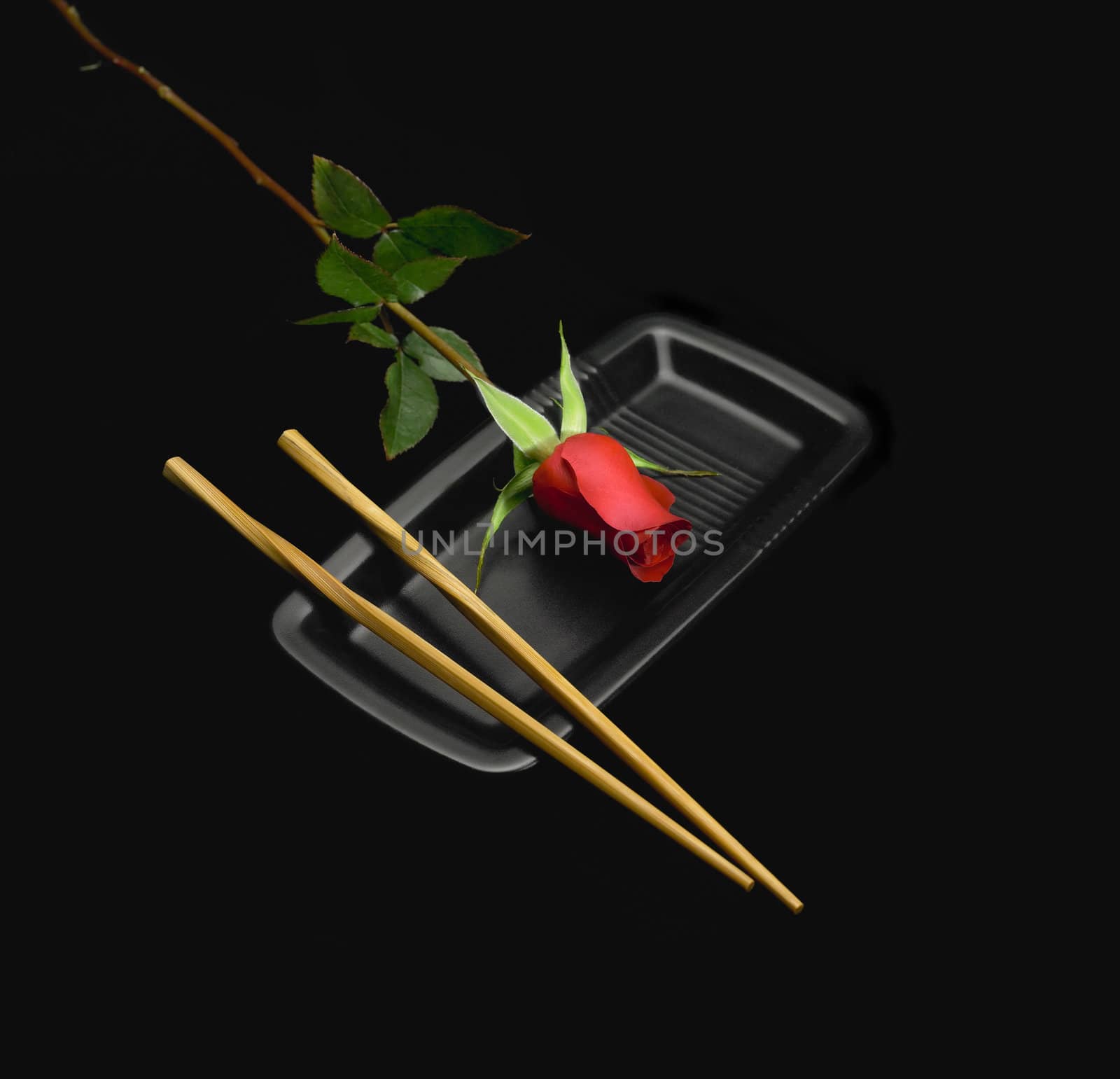 red rose on a japanese plate with chopstick over black background