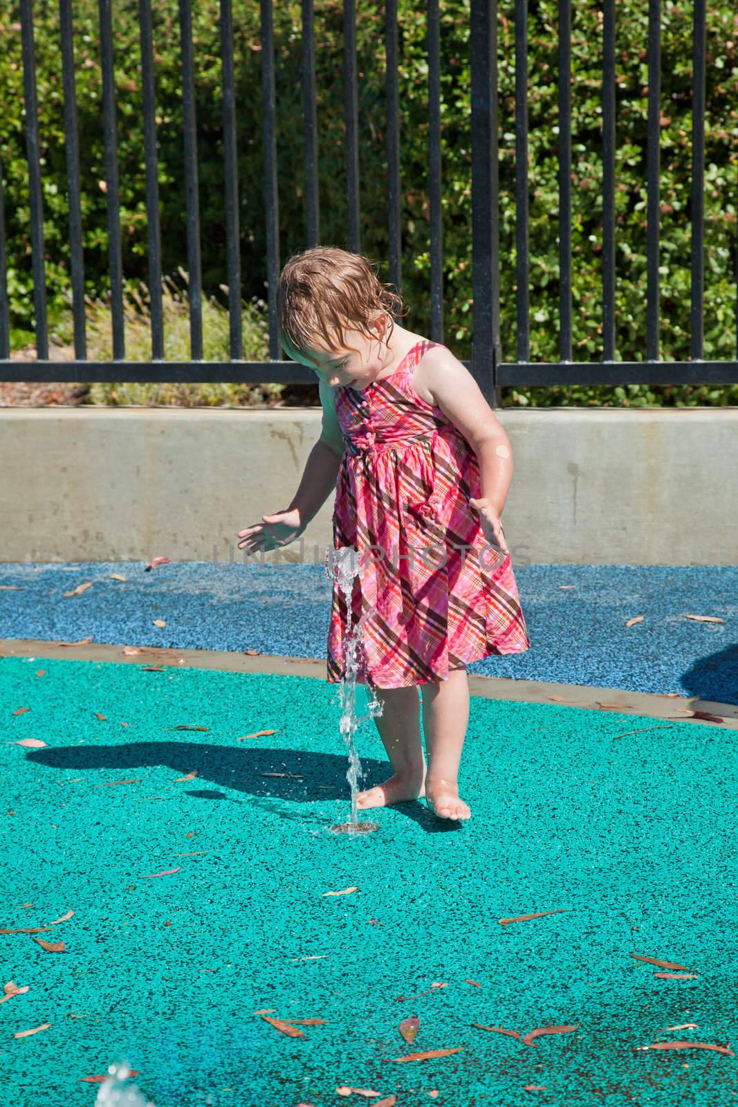 Cute little European toddler girl having fun with water at the playground in park