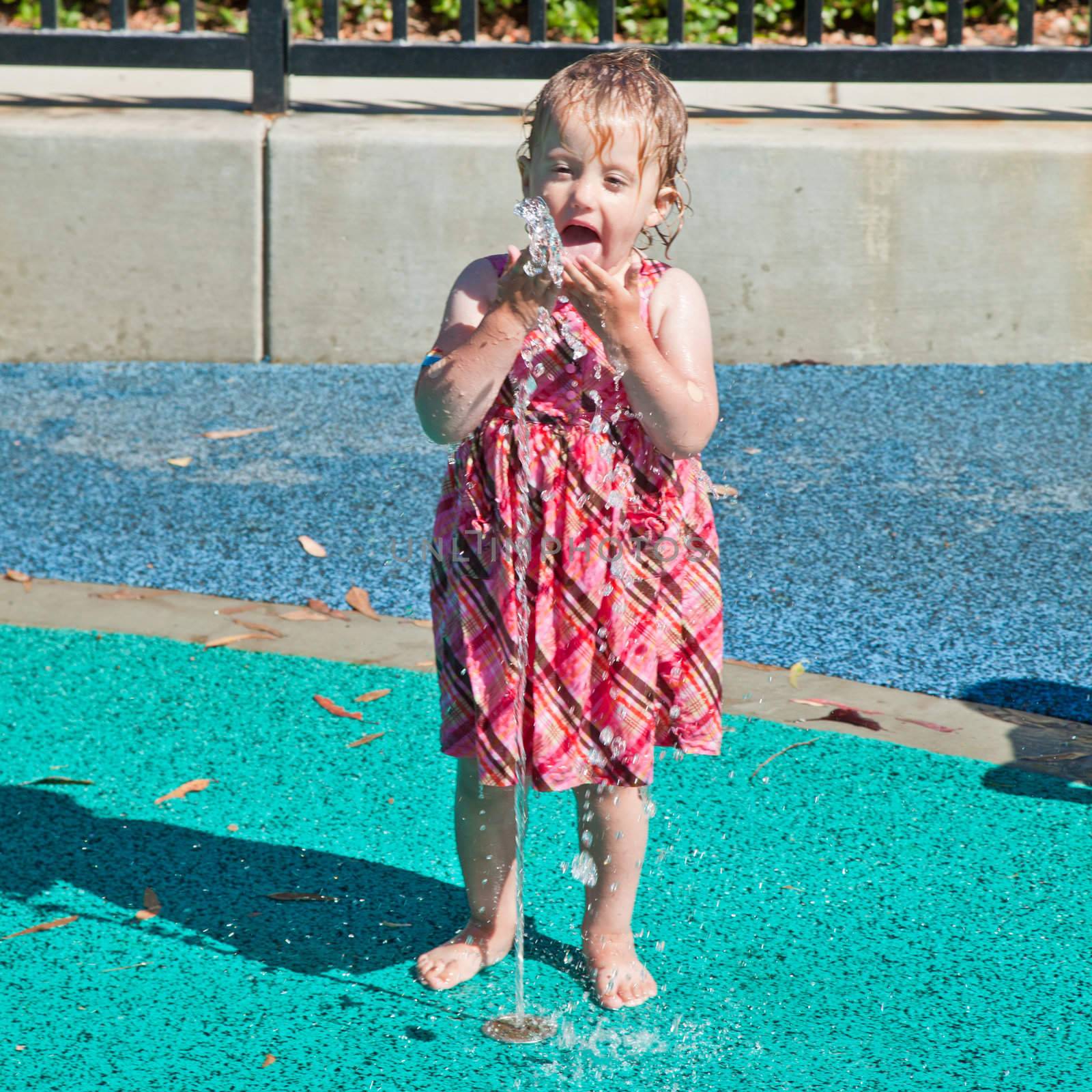 Cute little European toddler girl having fun with water at the playground in park