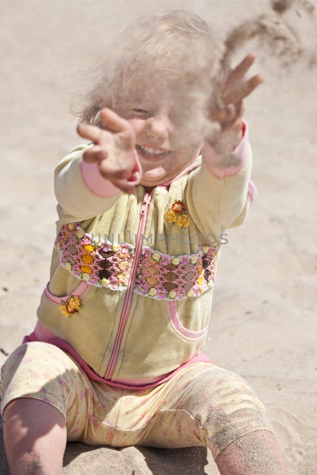 Cute little European toddler girl having fun with sand on the beach.