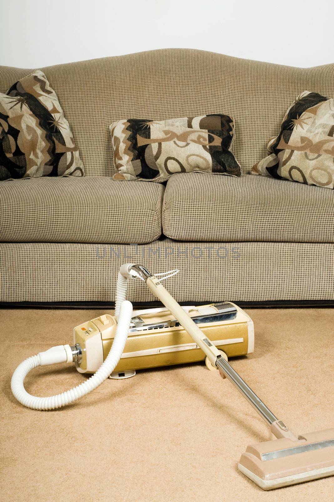 Cleaning house concept with an old canister vacuum and a plush sofa