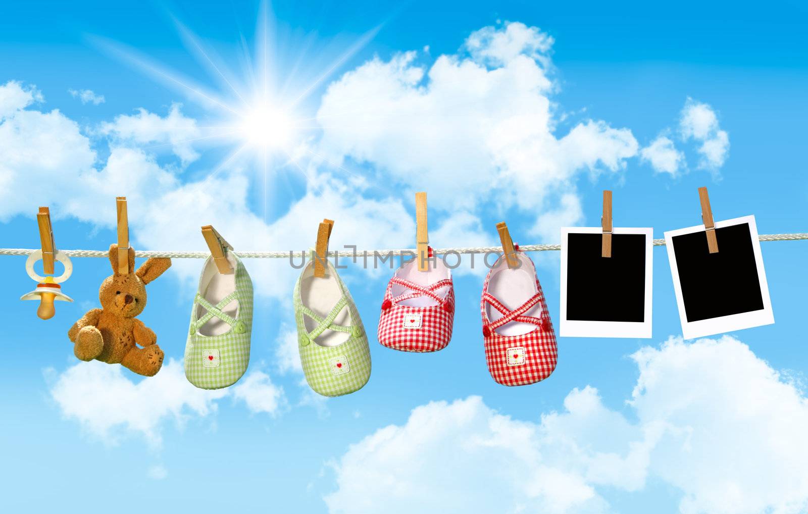 Baby shoes, pacifier and teddy bear on clothesline with blue sky