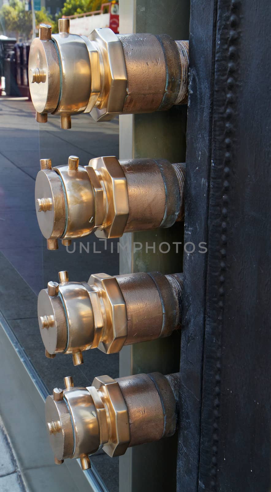 Four brass fire hose connections sticking out of a city building