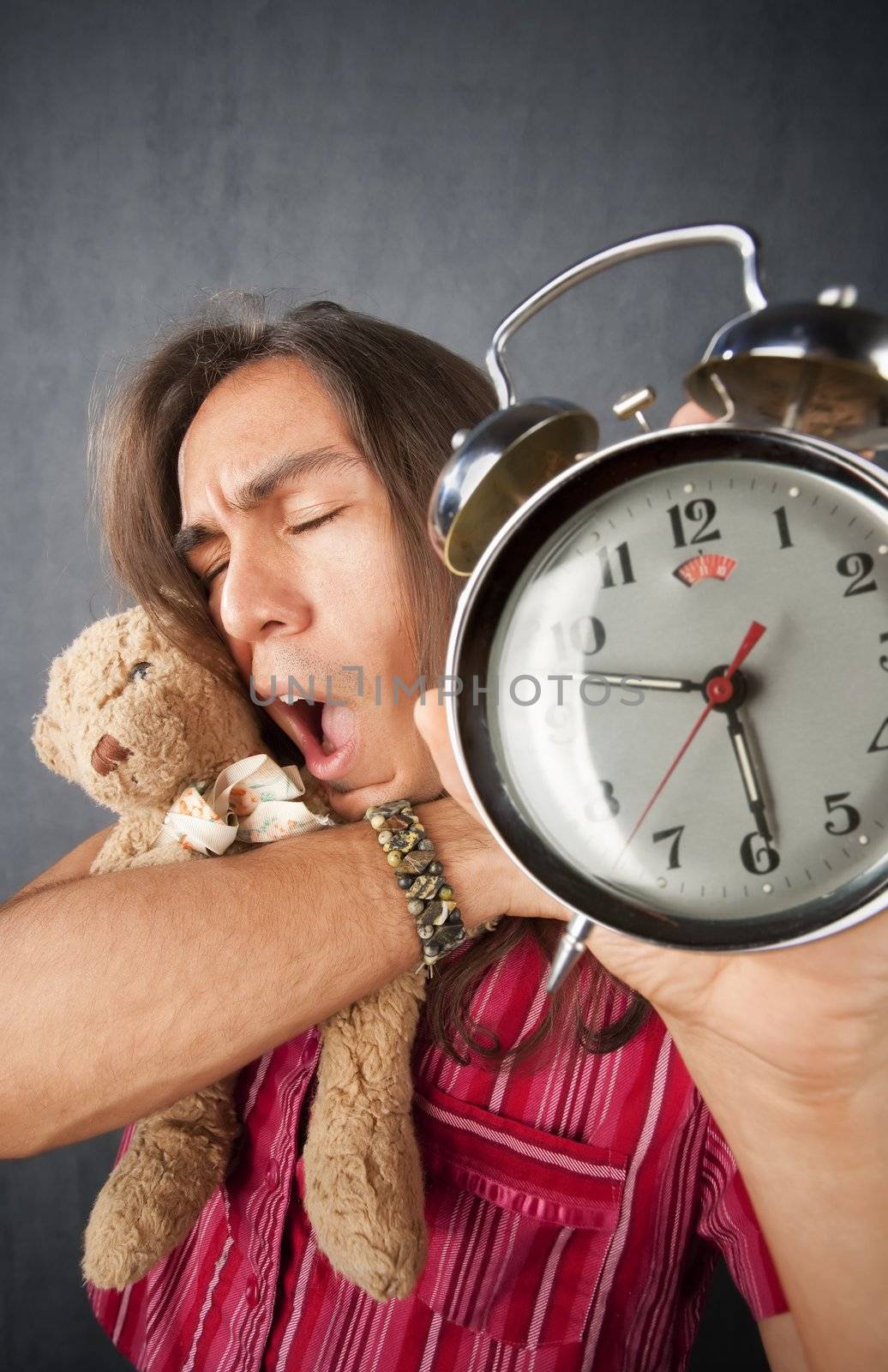 Sleepy handsome young man with long hair and alarm clock