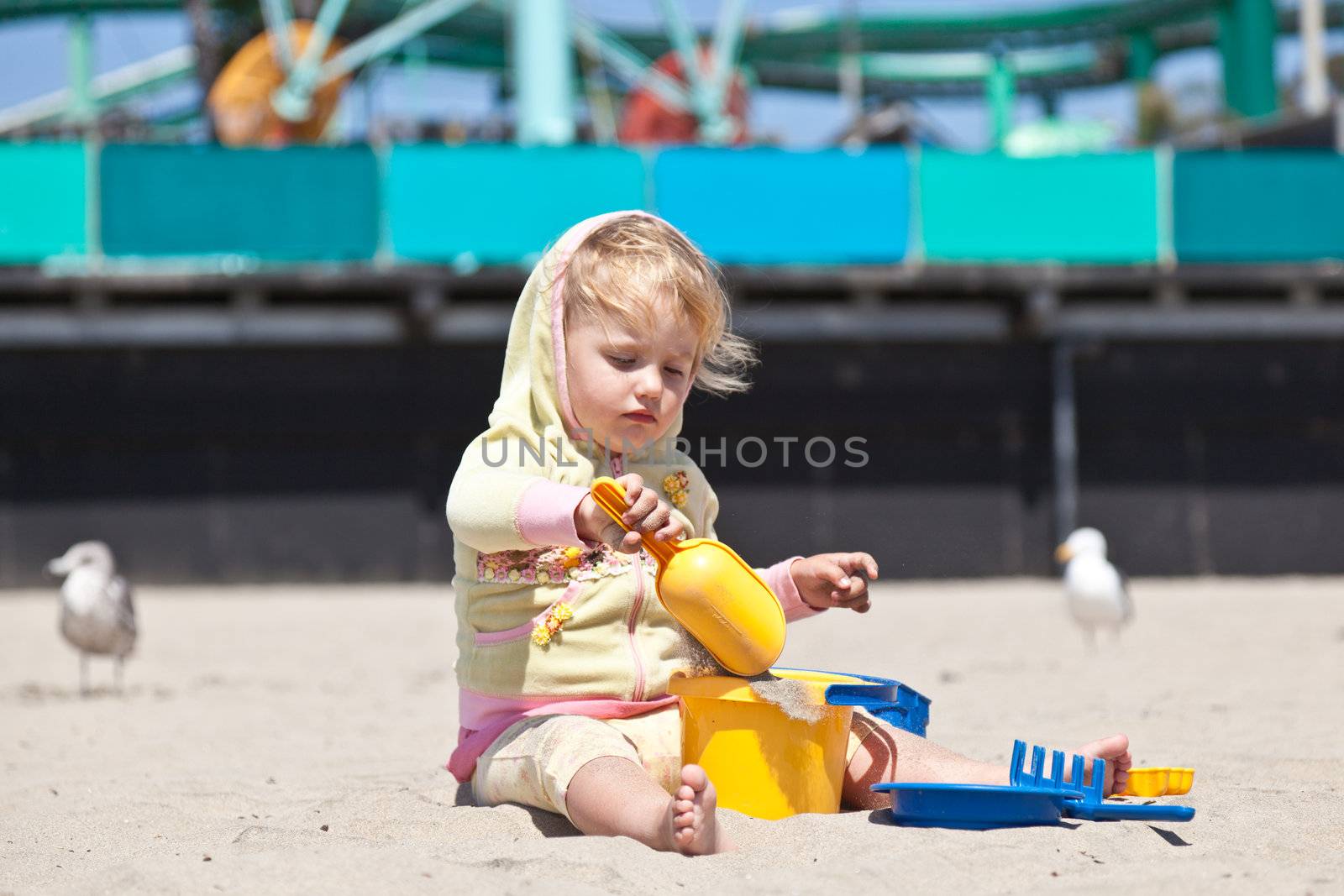 Cute little European toddler girl having fun with sand on the beach.