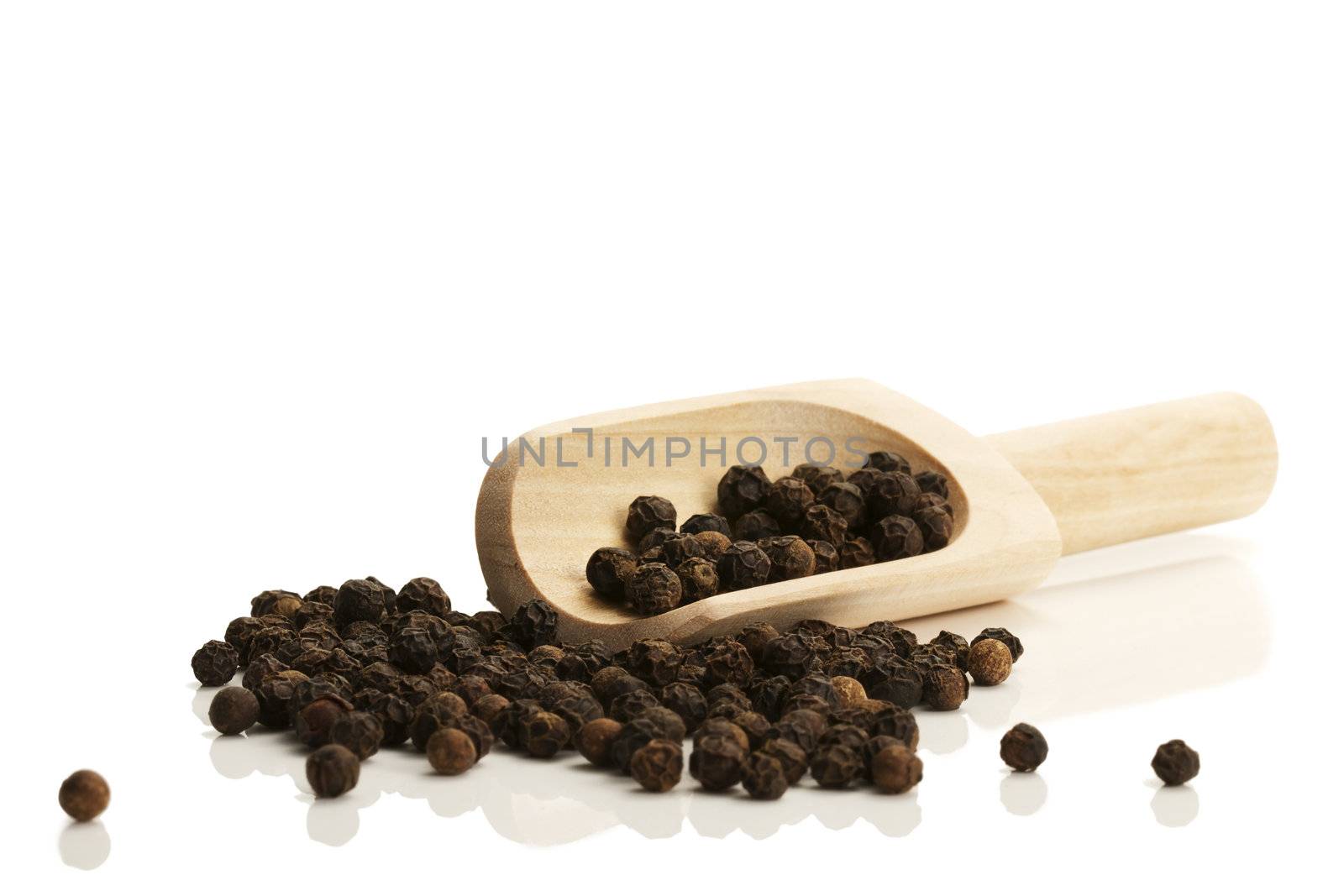 black peppercorns with a small wooden shovel from side on white background