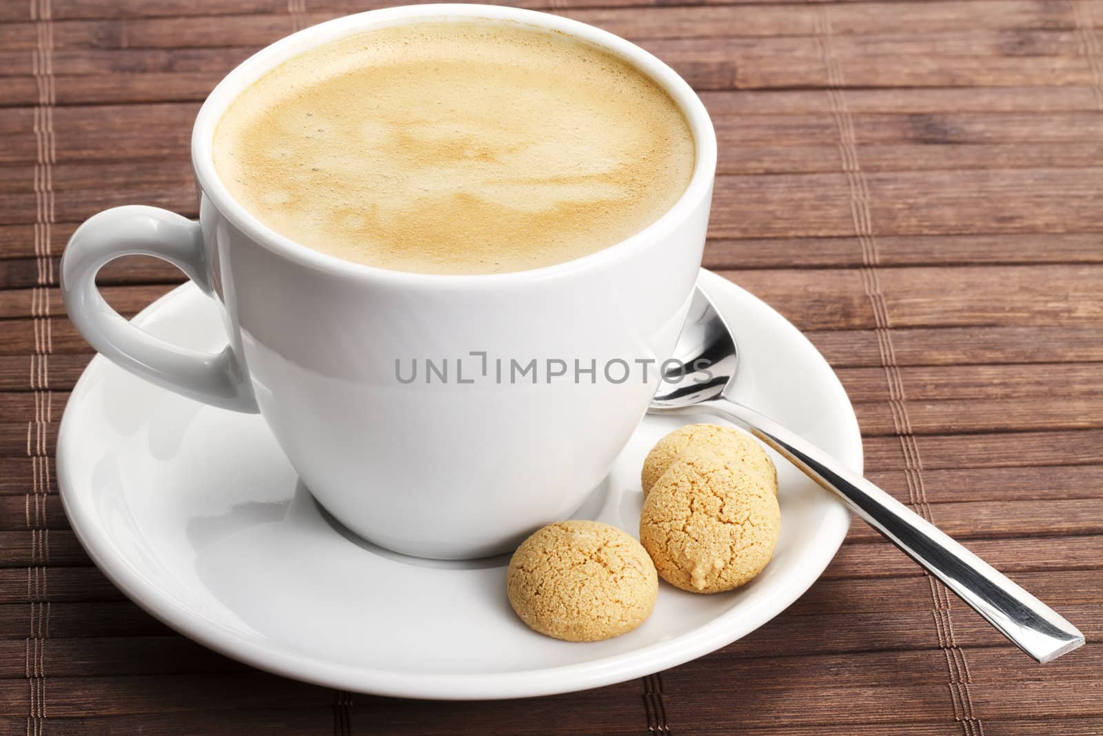 coffee in a white cup with amarettini and a spoon on wooden background