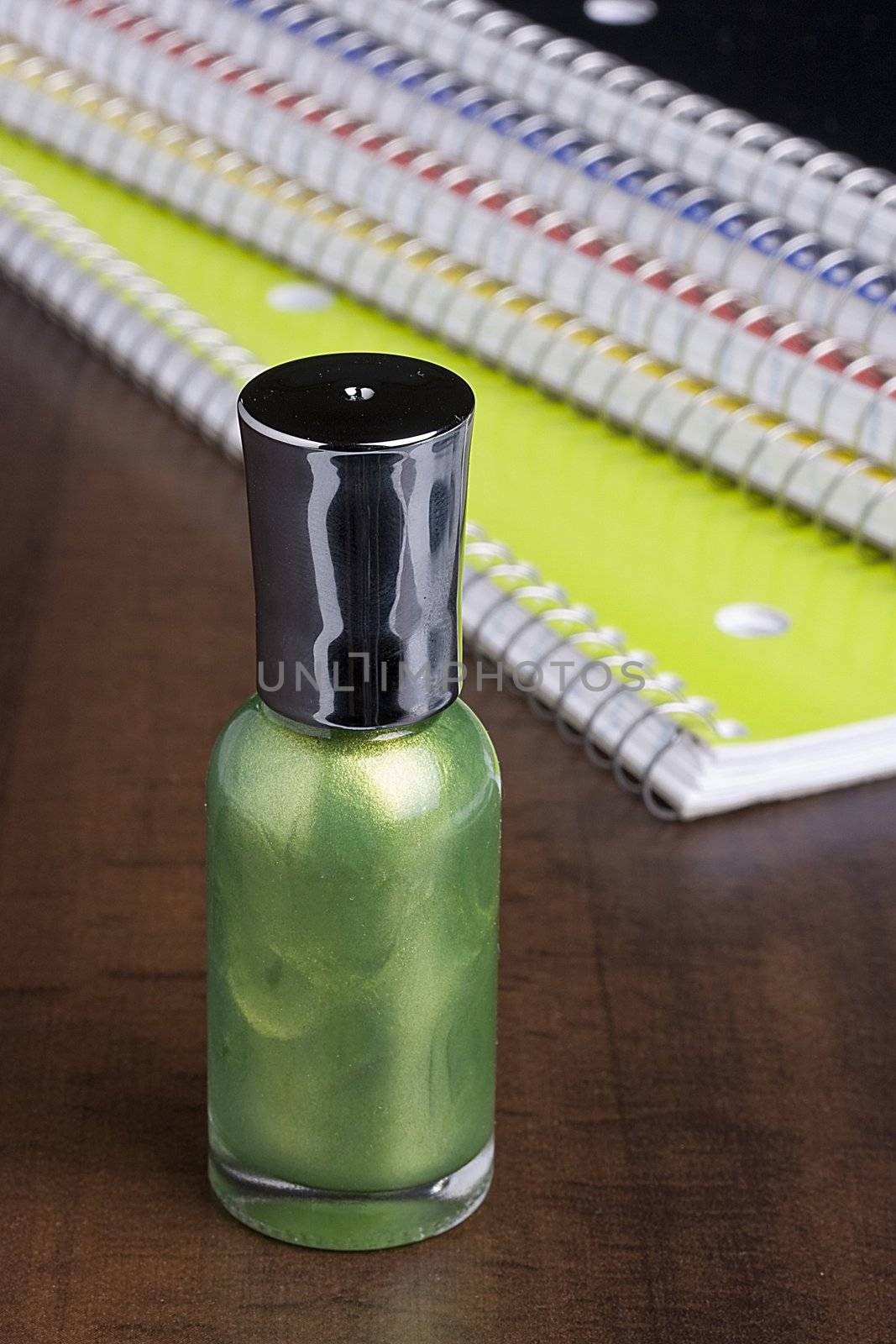 Green nail polish standing in front of a stack of notebooks.