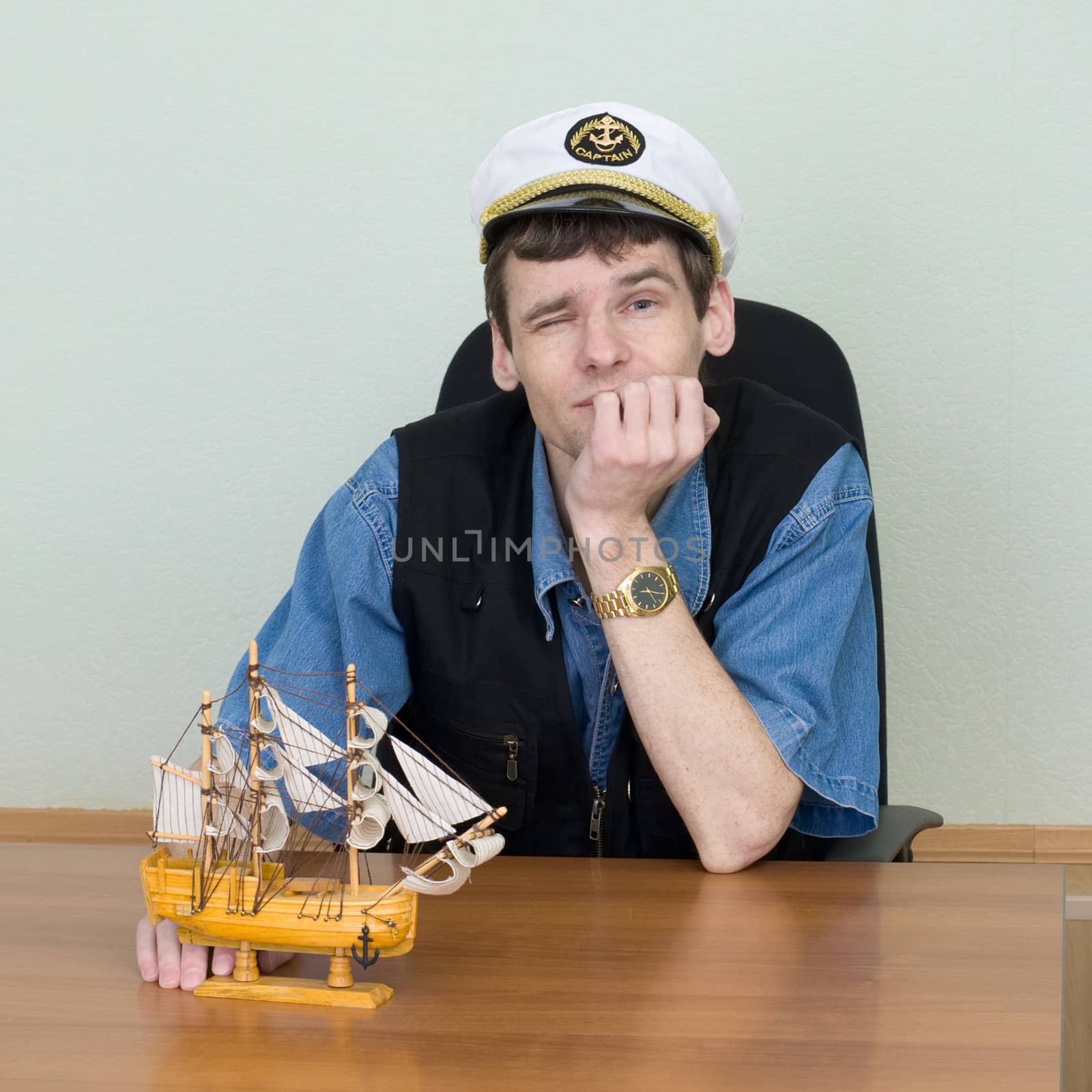 Man in a uniform cap at table with model of ship