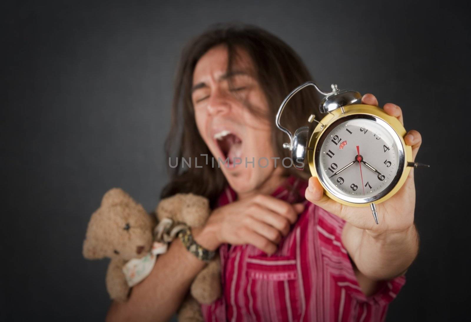 Sleepy handsome young man with long hair and alarm clock