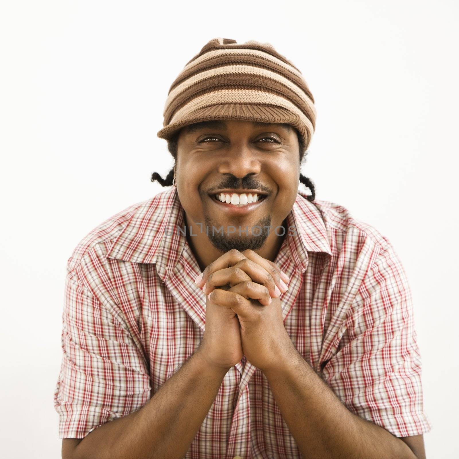 African-American mid-adult man wearing hat and smiling at viewer with hands together.