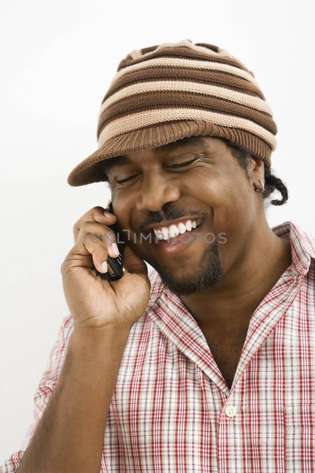 African-American mid-adult man wearing hat and smiling while talking on cell phone.